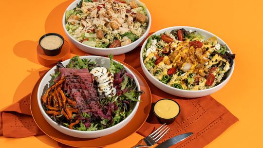 Three Boali salads with dressings on an orange table
