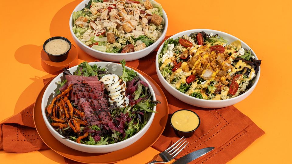 Three Boali salads with dressings on an orange table