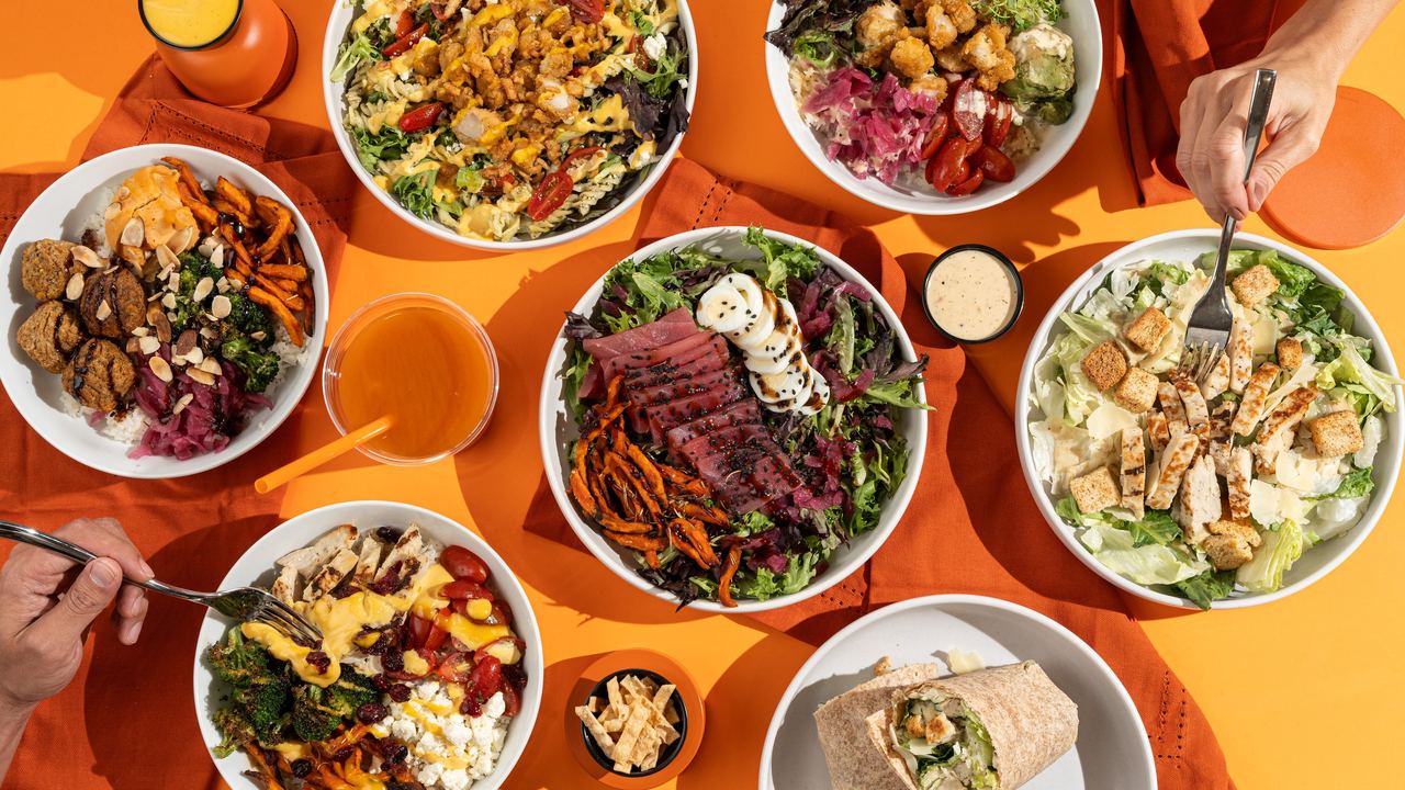 Boali bowls, salads and wraps on an orange table, seen from above