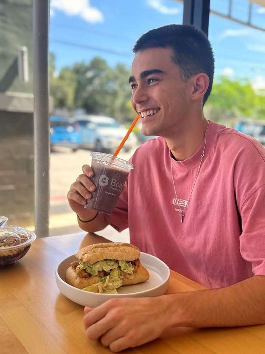 Guest smiling with a Boali shake and a sandwich at the Plantation restaurant