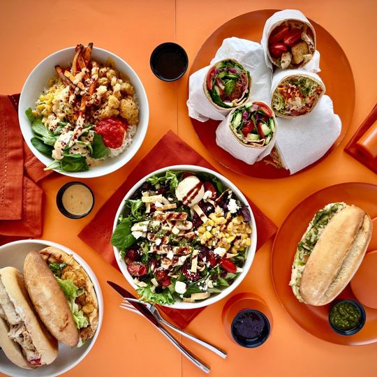 Boali sandwiches, wraps and a salad on an orange table